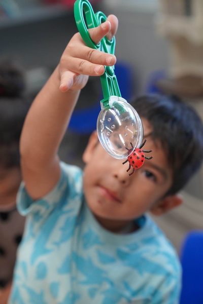 A young man holding a lady bug with plastic tongs